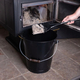 The ashes are putting on the black container using the black shovel to clean the fireplace.